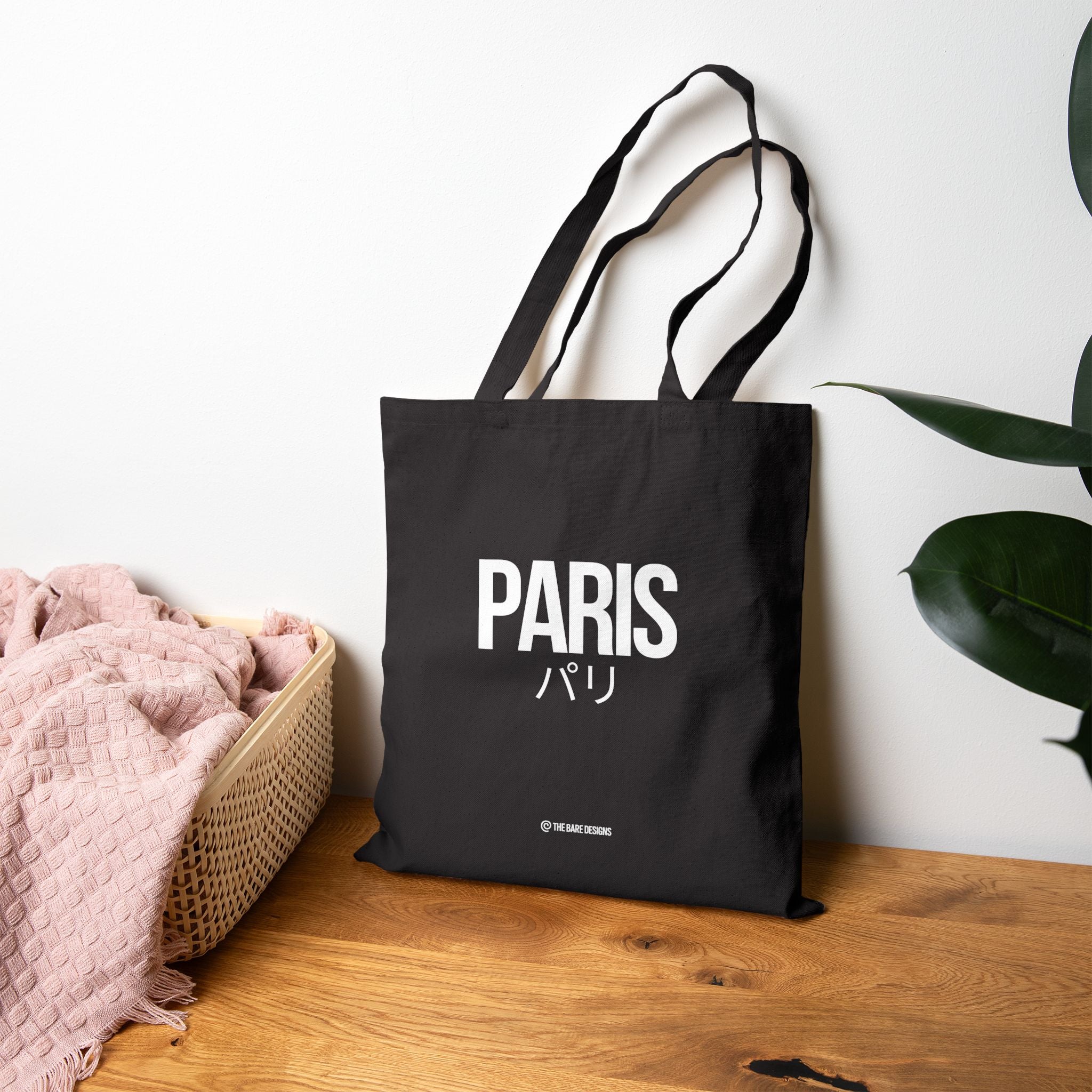 Black tote bag with 'PARIS' text on a wooden surface with a plant in the background