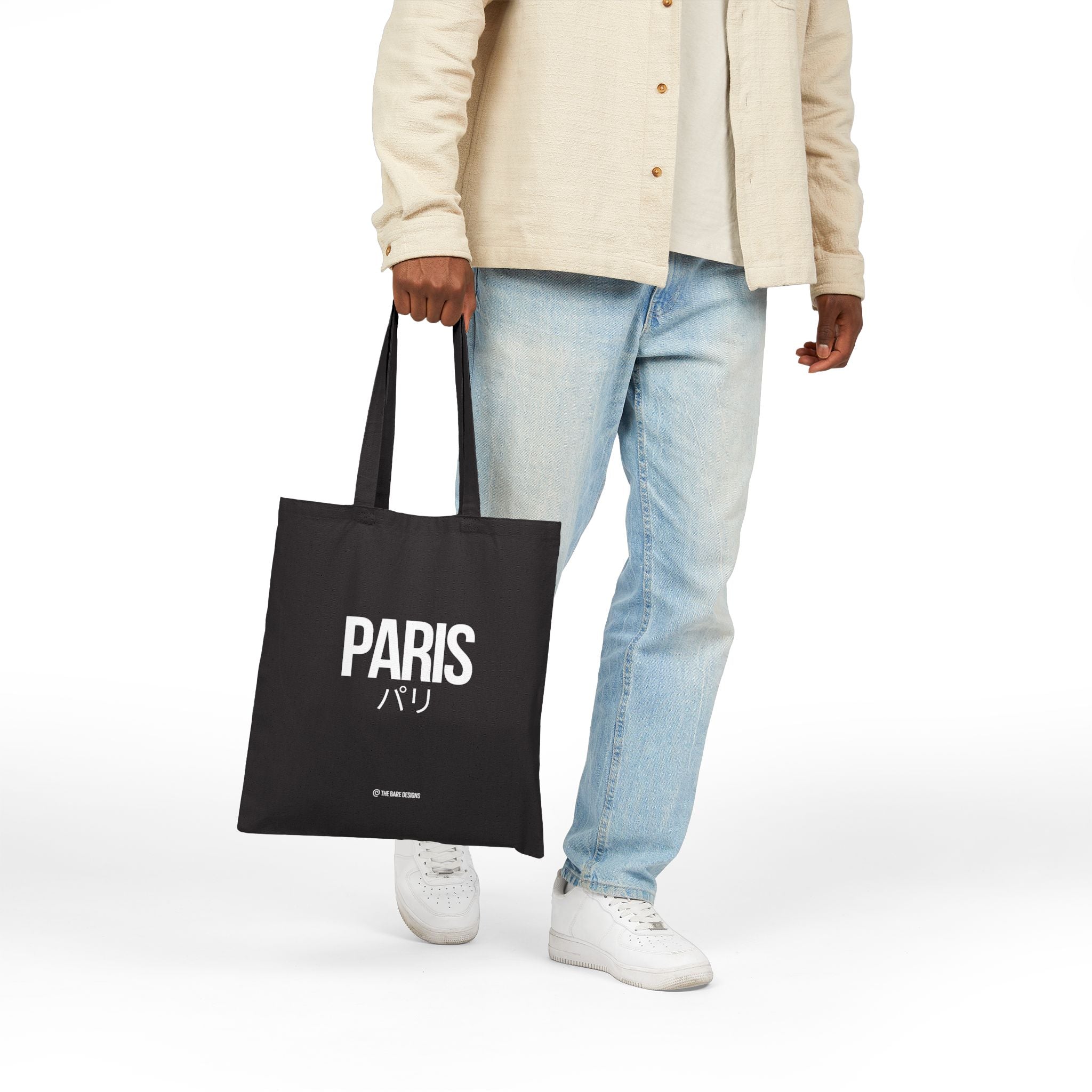 Black tote bag with 'PARIS' and Japanese characters printed on it.  Held by a man.