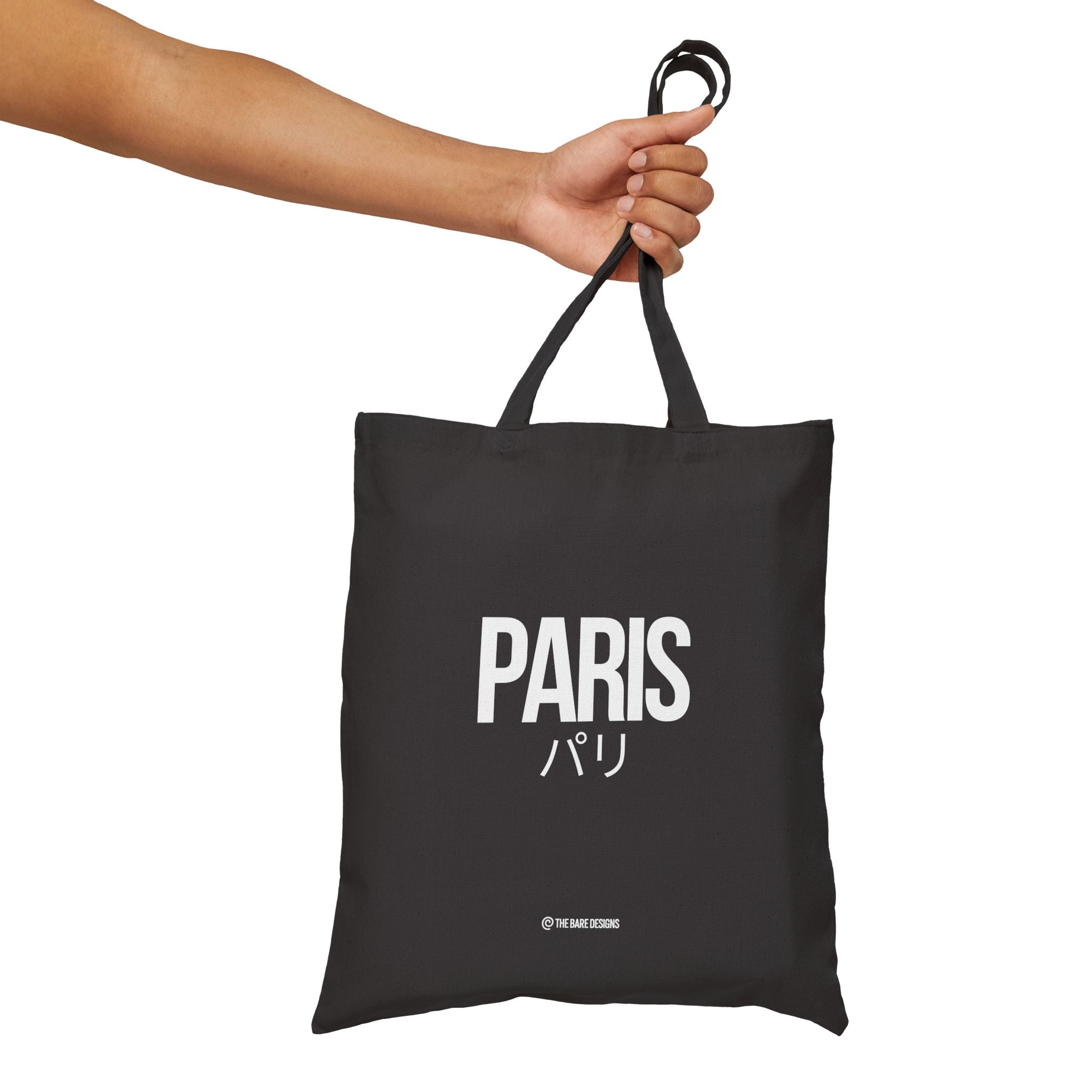 Black tote bag with 'PARIS' text held by a hand on a white background