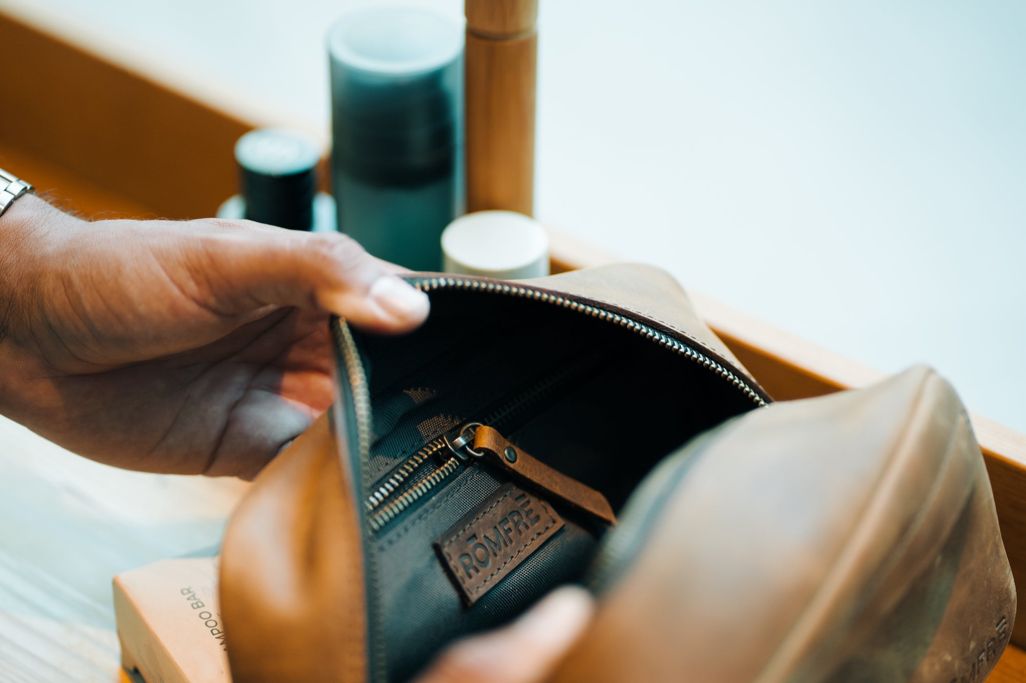 Person opening a beige leather bag with a brand logo, revealing its interior.