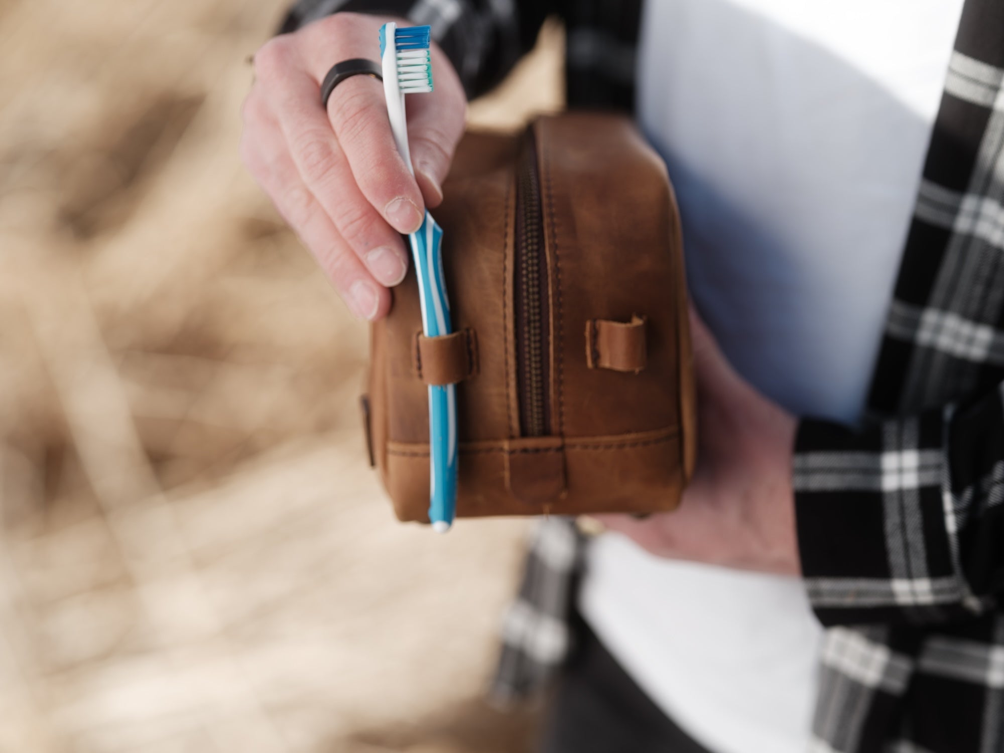 Person holding a brown leather toiletry bag with a toothbrush inside, blurred background