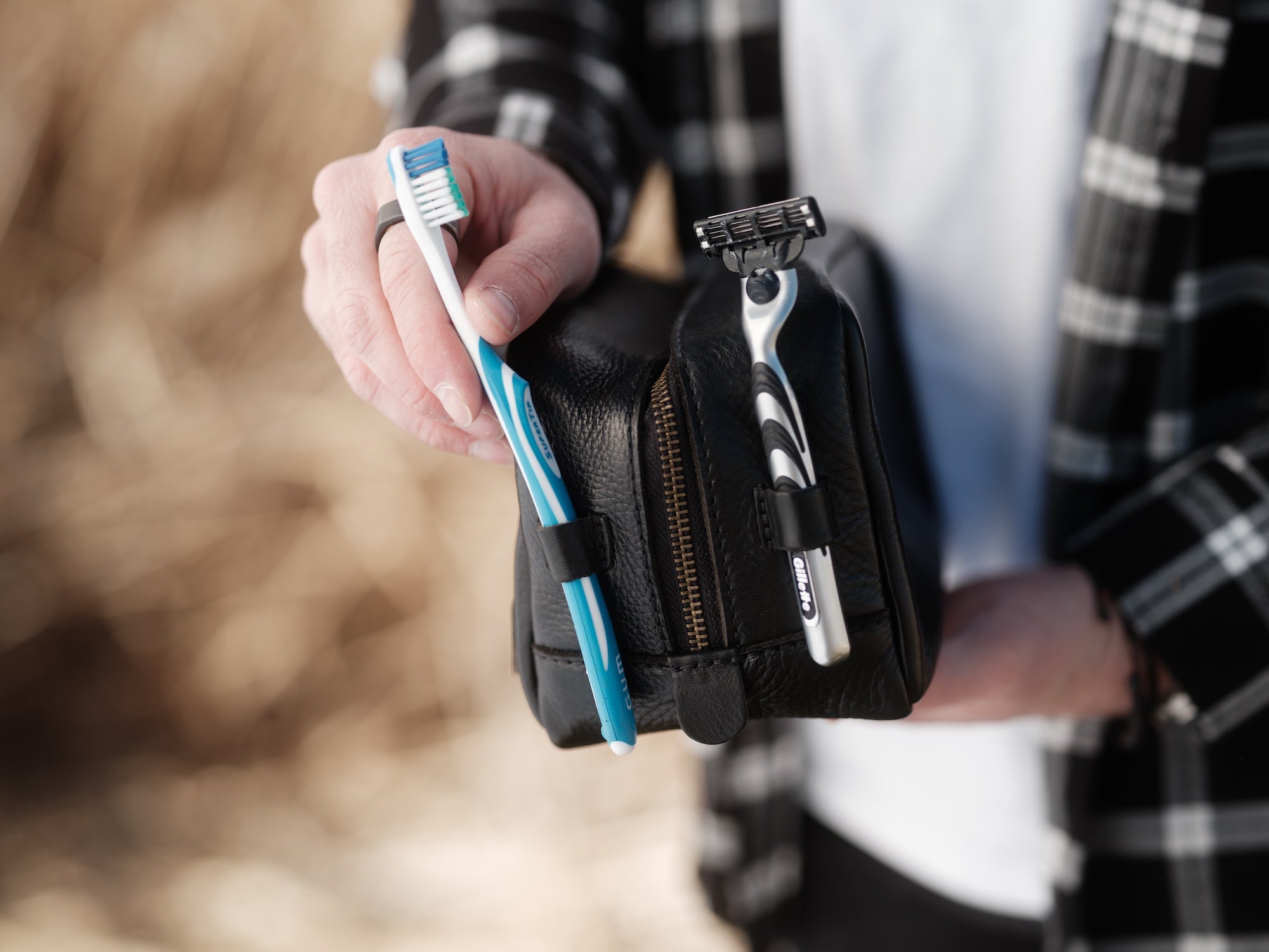 Person holding a black leather case with a razor and toothpaste, blurred background