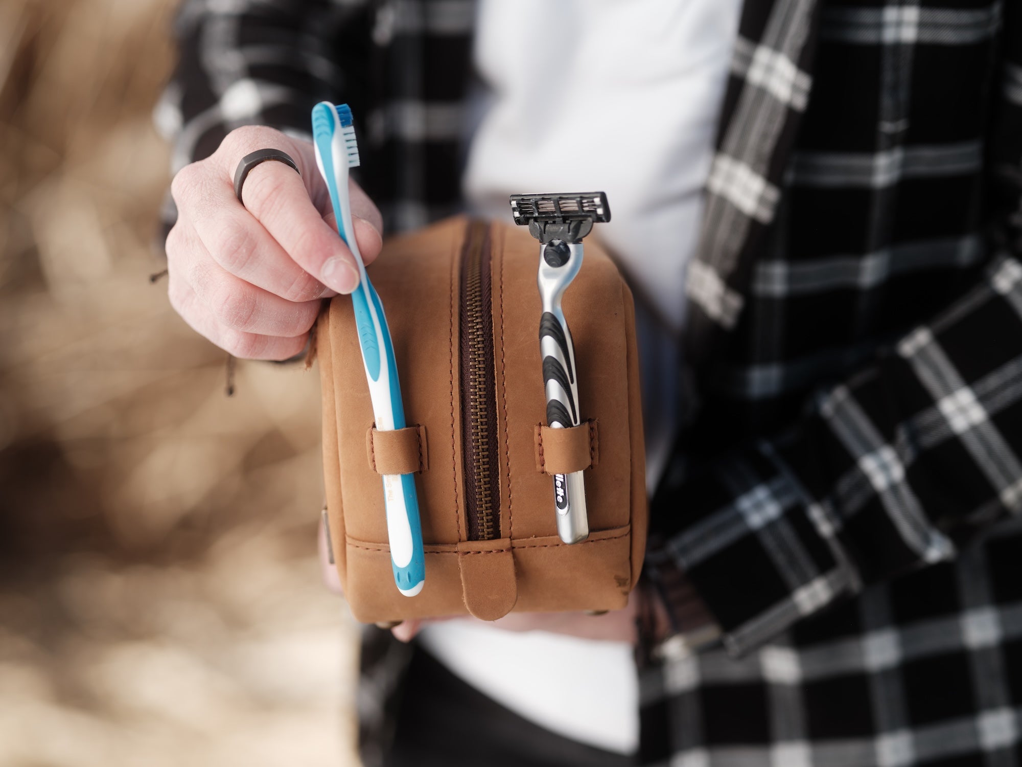Person holding a brown toiletry bag with a toothbrush and razor.