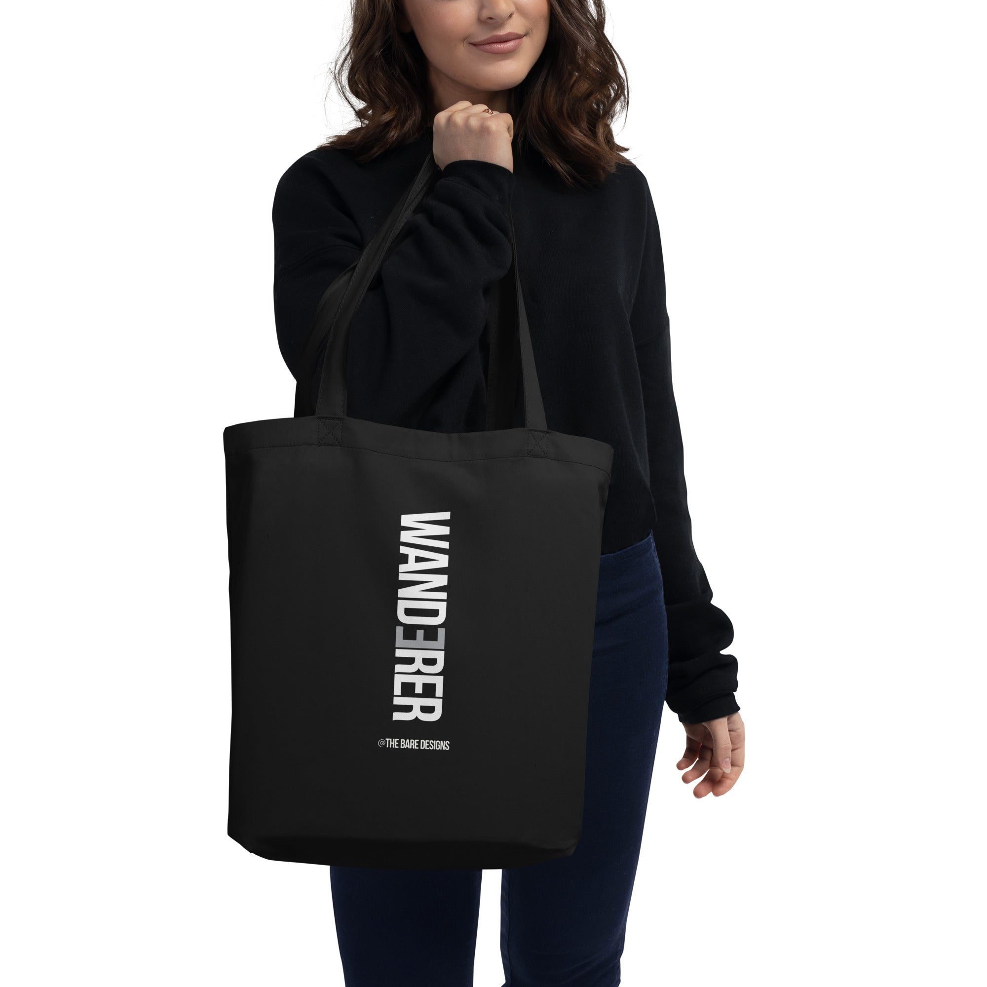 person holding a black tote bag with "wanderer" written in bold white lettering.  Designed by the bare designs